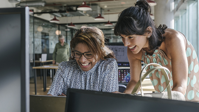 Two women smiling and working together in office setting