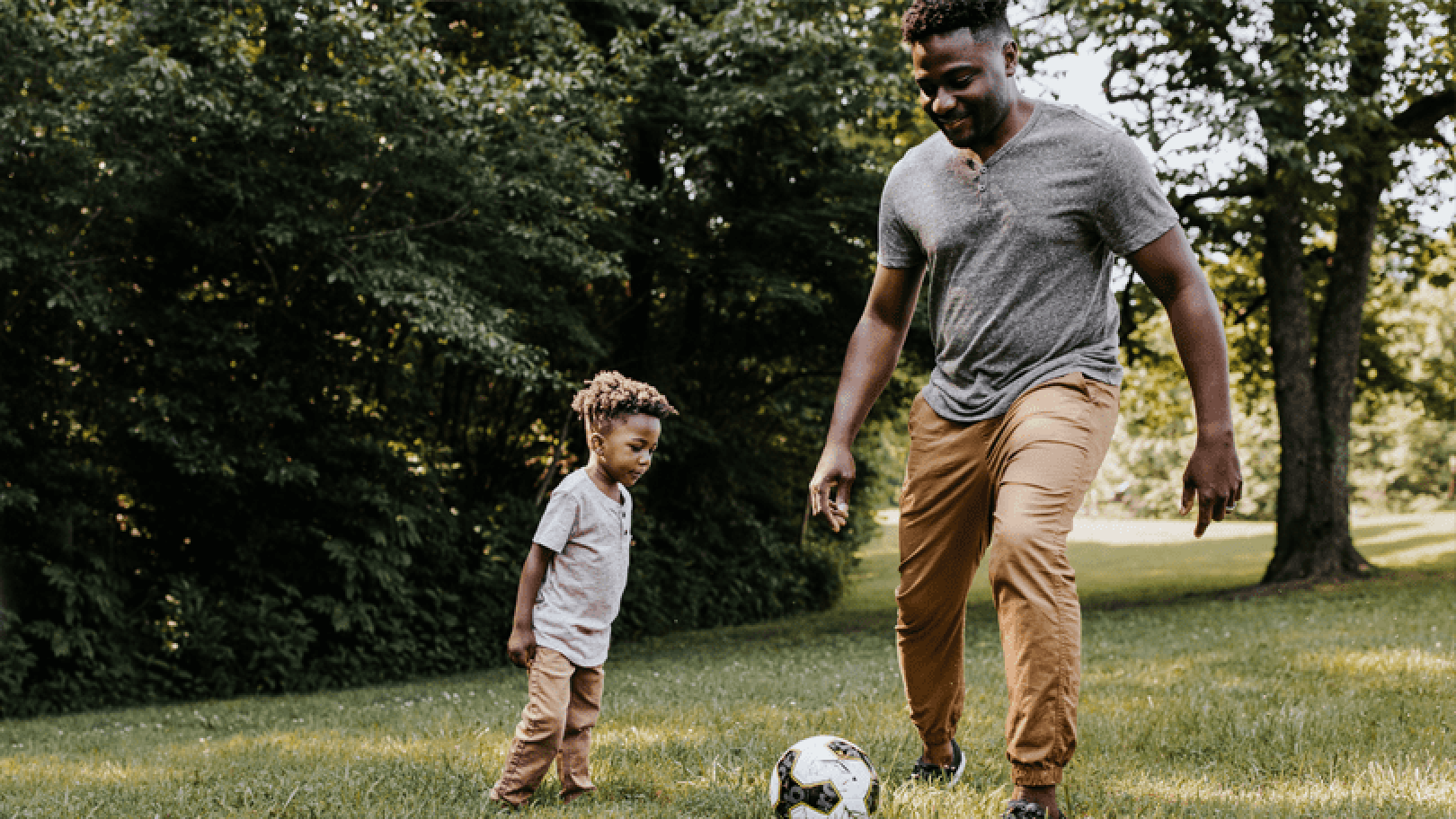 Father playing soccer with his young son outside