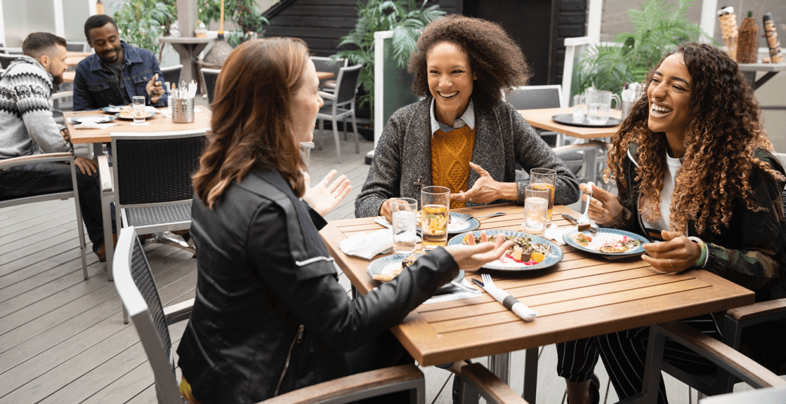 Friends laughing over lunch at outdoor restaurant