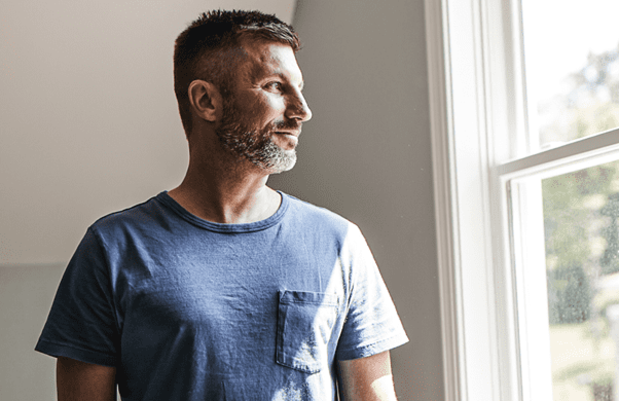 Man standing indoor and looking out a window