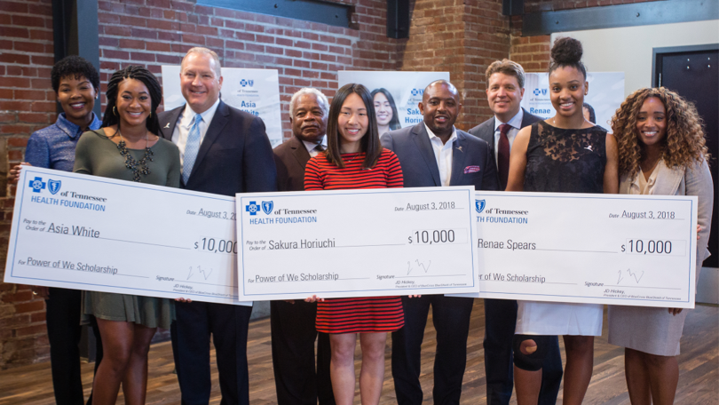 Leadership with minority students holding scholarship checks.
