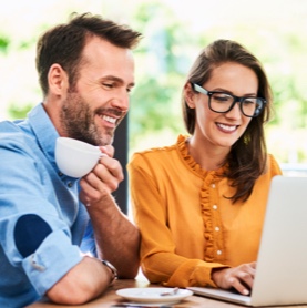 Two people smiling while working on a laptop