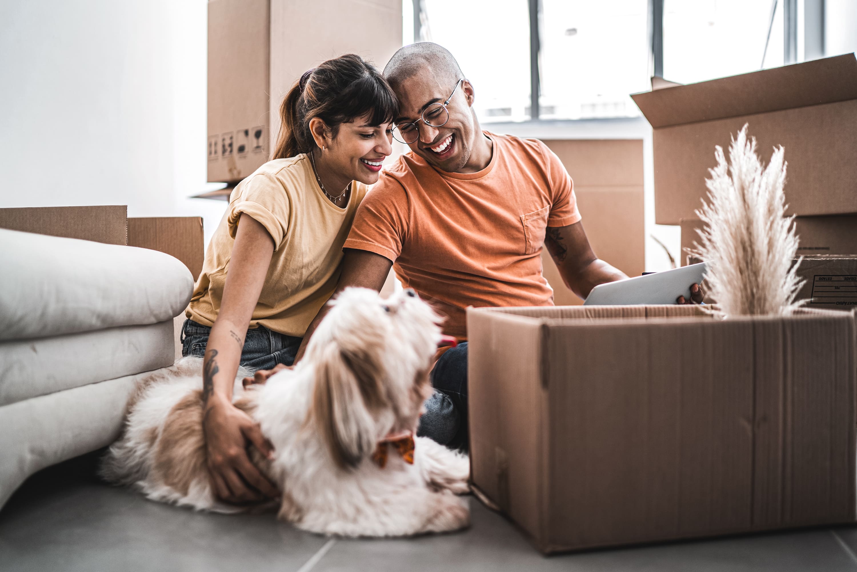 Smiling young couple with dog seated on floor surrounded by moving boxes