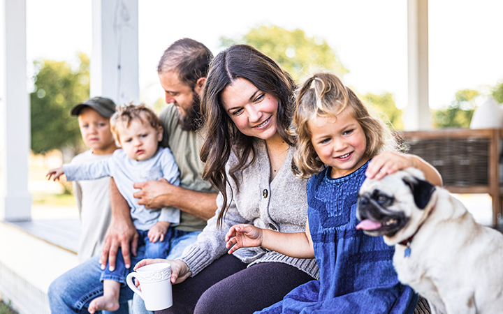 Family of mother, father, 3 children and a dog sitting on a porch
