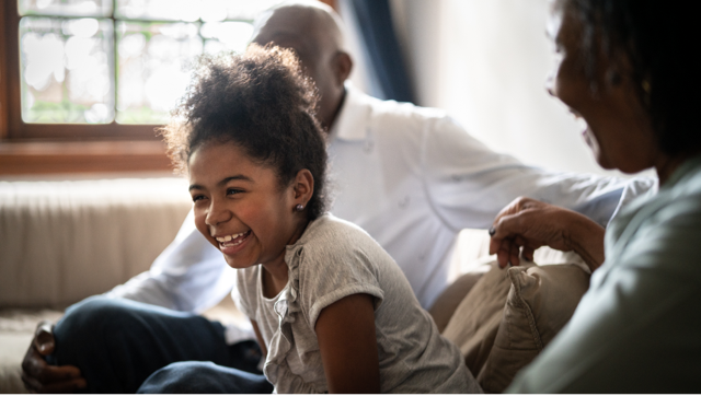 Young child laughing at her parents while sitting on couch Young child laughing at her parents while sitting on couch