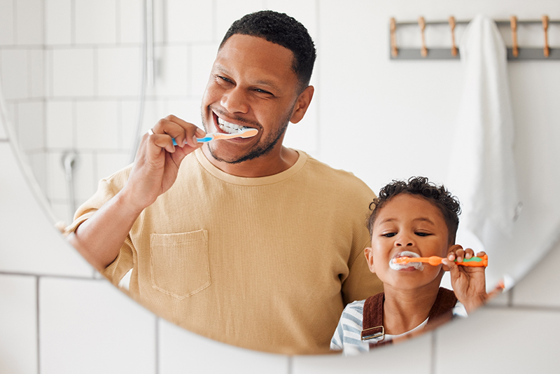 Father and young son brushing their teeth together in a bathroom