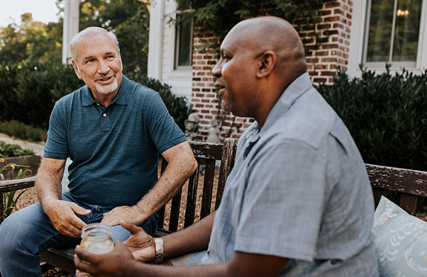 Two men talking and sitting outside in garden chairs.