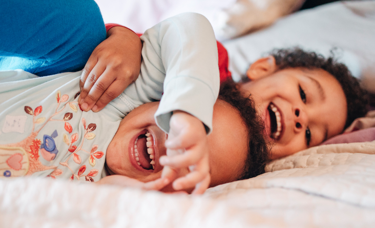 A brother and sister wearing pajamas excitedly laughing and hugging on a bed