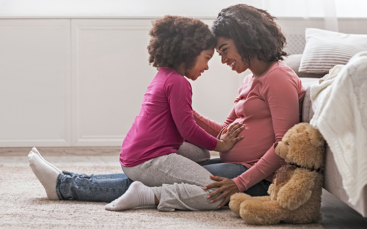 Smiling mother with her toddler happily resting on her pregnant belly