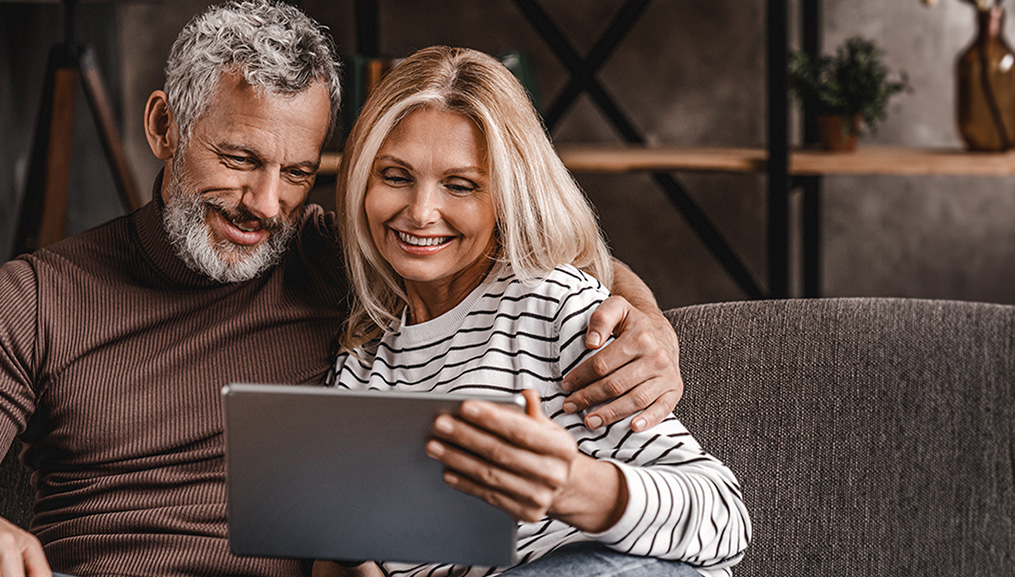 A couple using their tablet while sitting on their couch.