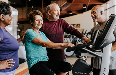Two older couples talking as they work out at the gym.