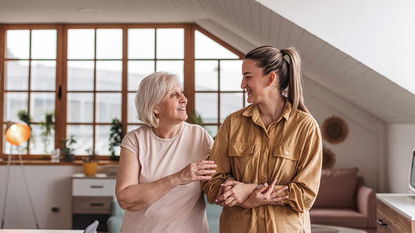Mother and daughter with arms linked standing in their living room.