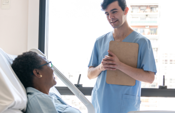 Male medical staff with clipboard, talking to patient in hospital bed | BCBS of Tennessee
