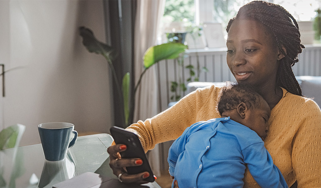Younger mother holding her sleeping baby while looking at her phone Younger mother holding her sleeping baby while looking at her phone